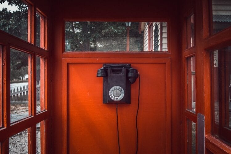 black rotary telephone mounted on red wooden wall