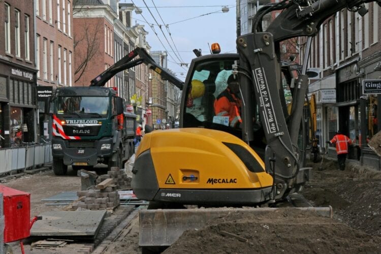 person using heavy equipment near vehicles, people, and buildings